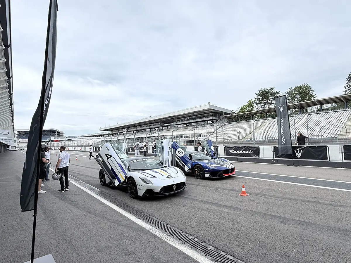 Ein weisser und ein dunkelblauer Maserati GT2 Stradale mit weit geöffneten Schmetterlingstüren parkieren nebeneinander auf dem Asphalt des Hockenheimrings.