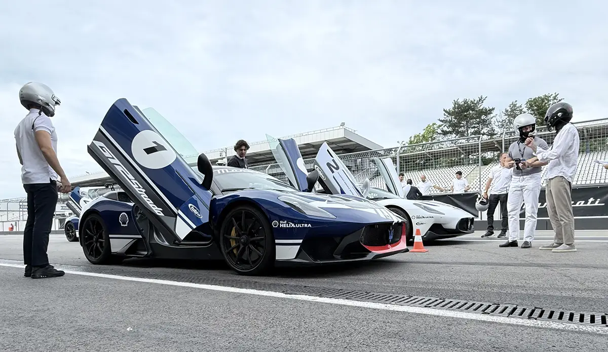 Ein Instruktor im Maserati-Fahrerlager bespricht Details mit einem Teilnehmer im weissen Rennanzug direkt neben einem dunkelblauen Maserati GT2 Stradale mit der Startnummer 1.
