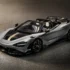 Silver McLaren 720S Spider convertible with a gold racing stripe, shown from the front-left on a textured asphalt surface. The car features a large rear wing and tan interior seats visible through the open top.