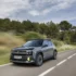 Blue-gray Renault SUV driving on a rural two-lane road with trees and blue sky ahead of it