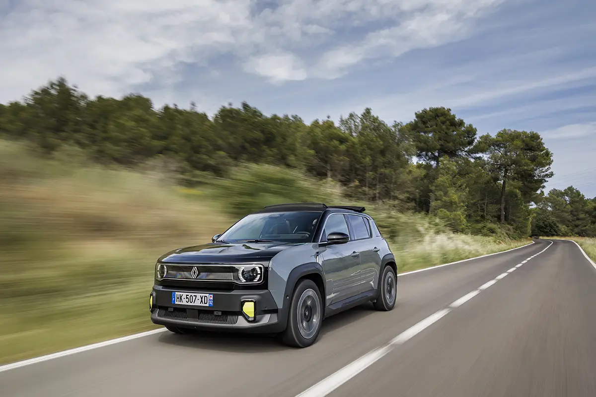 Blue-gray Renault SUV driving on a rural two-lane road with trees and blue sky ahead of it