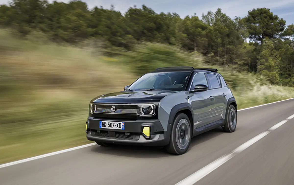 Ein grauer Renault 4 E-Tech Electric fährt auf einer asphaltierten Landstrasse durch eine grüne Hügellandschaft.
