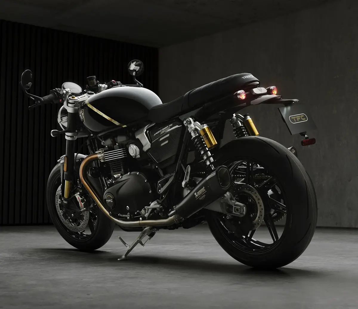 Side view of a black sport motorcycle parked indoors, highlighting its gold forks, exposed engine, and sleek exhaust.