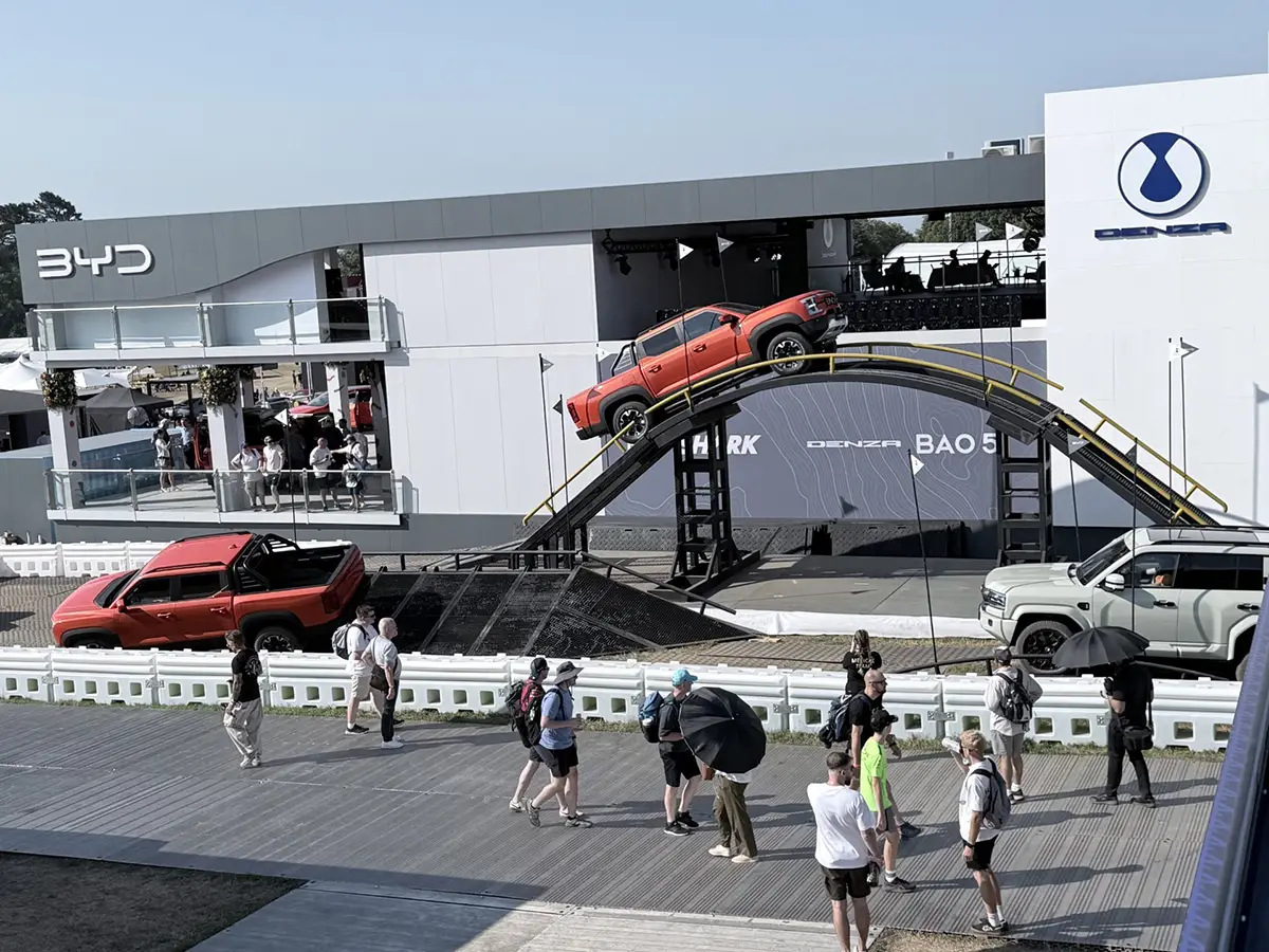 Großer BYD und Denza Messestand in Goodwood mit einer spektakulären, bogenförmigen Fahrrampe, auf der ein rotes SUV-Modell steht.