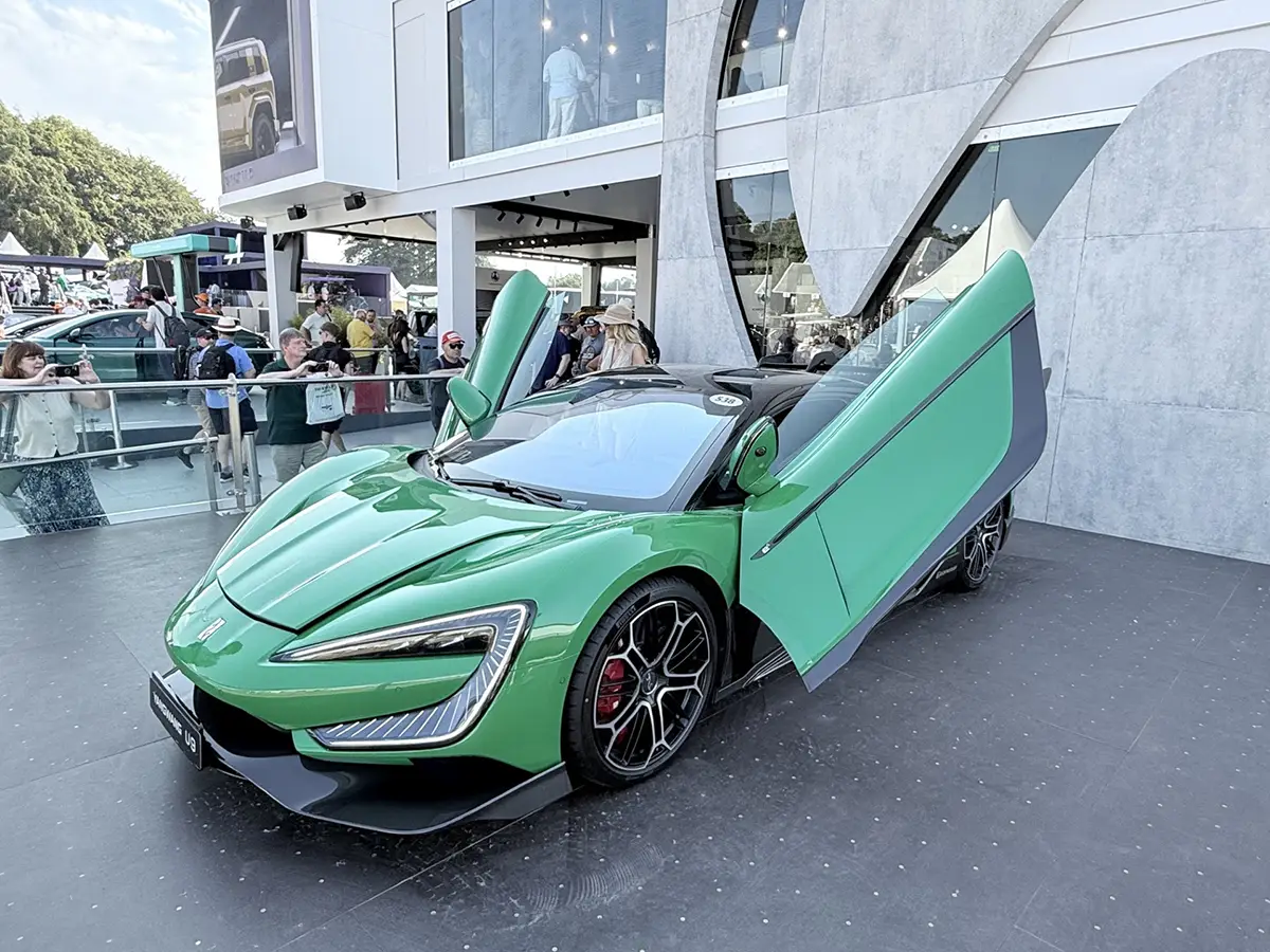 Ein moderner, giftgrüner Supersportwagen aus China präsentiert sich mit weit geöffneten Scherentüren auf dem Festivalgelände.