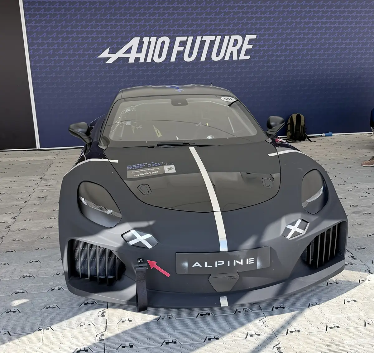 Der mattschwarze Elektro-Sportwagen-Prototyp Alpine A110 Future präsentiert auf der Ausstellungsfläche vor einer blauen Markenwand in Goodwood.