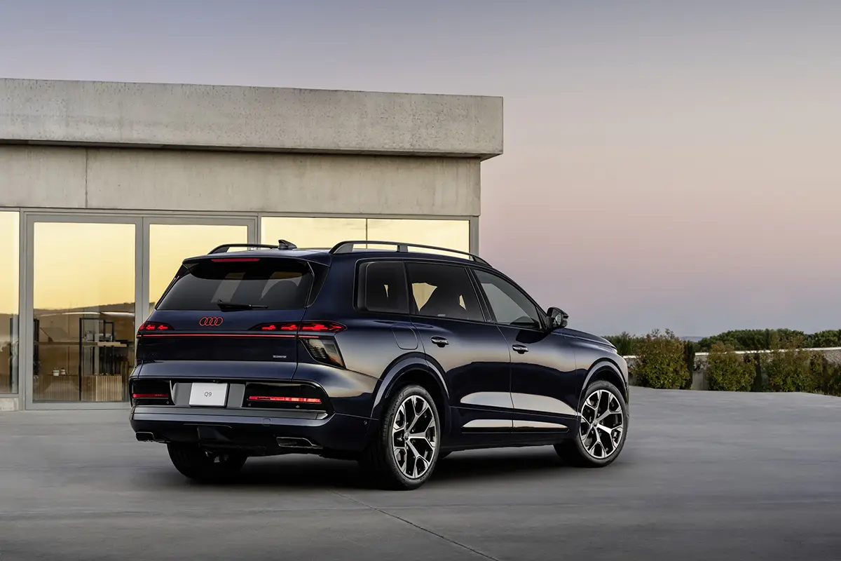Heckansicht des Audi Q9 mit durchgehendem OLED-Rückleuchtenband und leuchtenden Audi-Ringen bei Dämmerung.