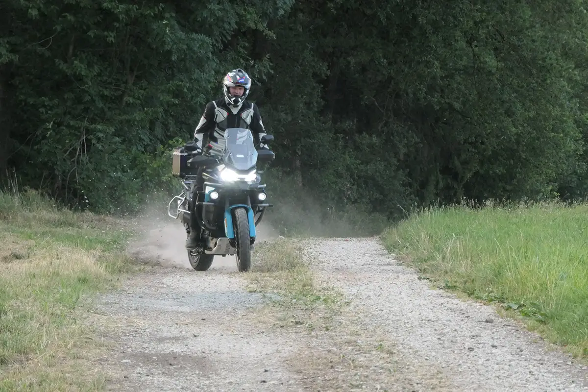 Frontal-Fahraufnahme der CF Moto 800 MT-ES mit eingeschalteten LED-Zusatzscheinwerfern auf einem Waldweg.