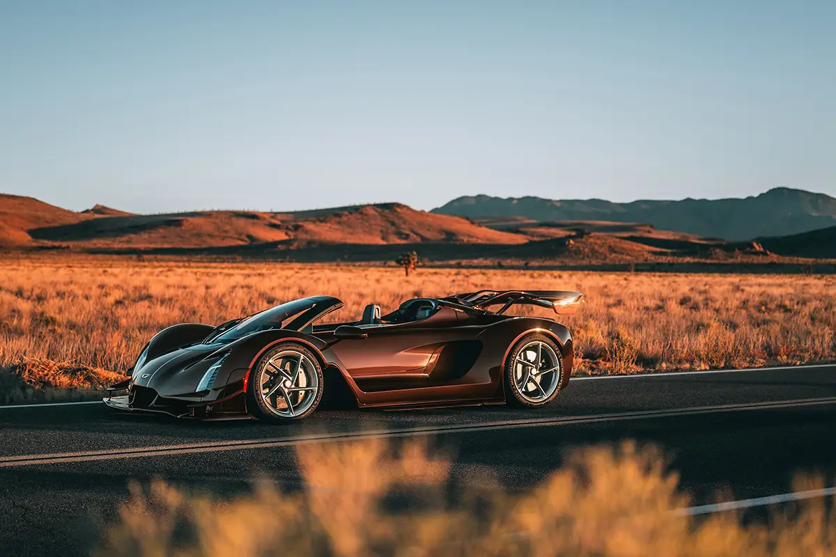 Seitenprofil des flachen Czinger 21C Spyder Hypercars auf einer Landstrasse vor einer Hügellandschaft.