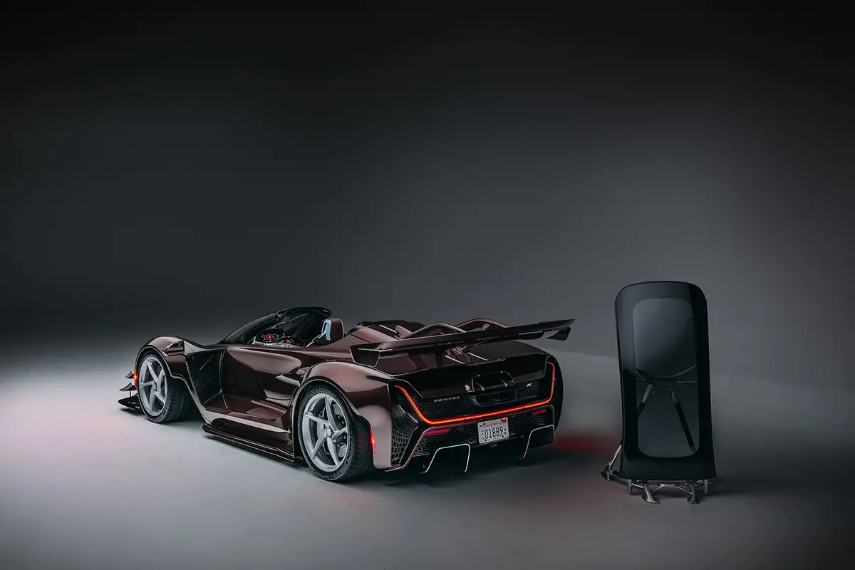 Heckdreiviertelansicht des Czinger 21C Spyder im Studio neben dem abgenommenen Carbon-Hardtop auf einem Spezialständer.