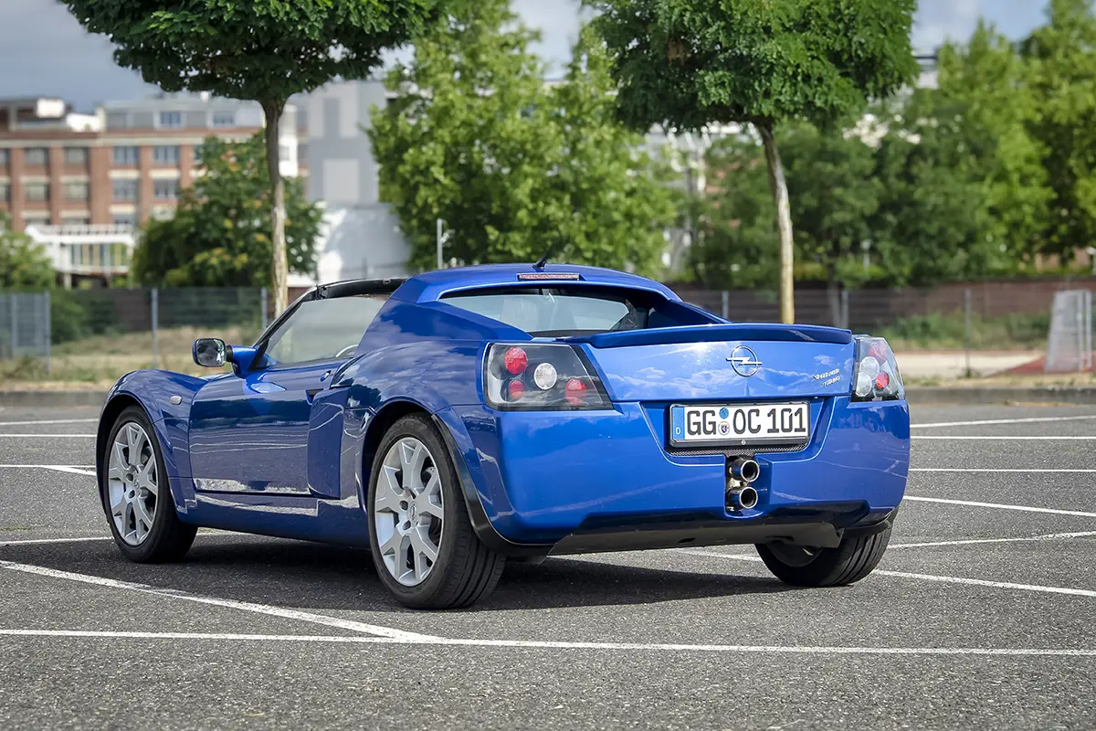 Heckansicht des blauen Opel Speedster mit doppelten Mittelendrohren auf einem Parkplatz.