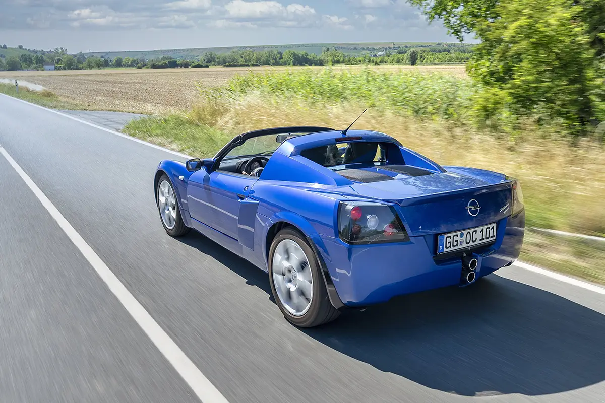 Heck-Dreiviertelansicht des blauen Opel Speedster beim Durchfahren einer leichten Kurve.