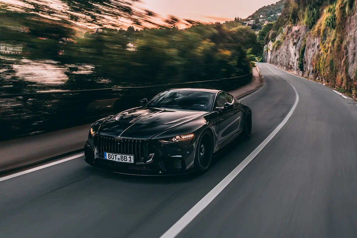 Dynamische Fahraufnahme des Brabus Bodo V12 Coupés auf einer kurvigen Küstenstrasse entlang steiler Felswände.