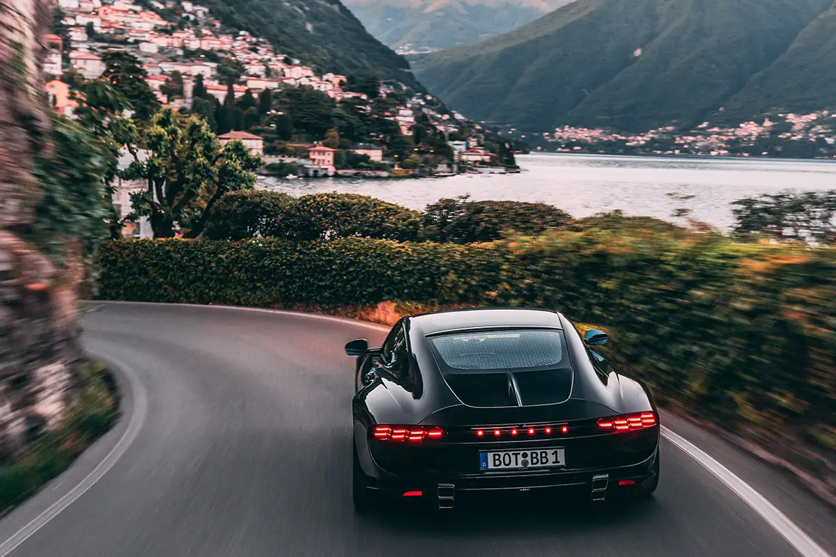 Heckansicht des tiefschwarzen Brabus Bodo bei der Fahrt auf einer Bergstrasse mit Blick auf eine Bucht.