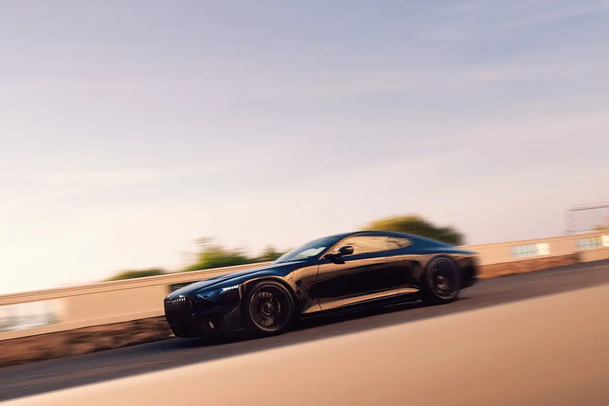 Seitenprofil des über fünf Meter langen Vollcarbon-Sportwagens Brabus Bodo in schneller Vorbeifahrt im warmen Abendlicht.