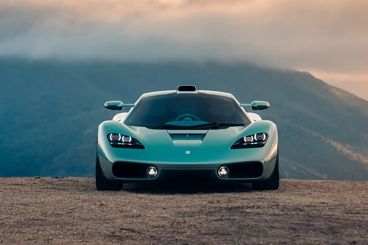 Frontalansicht des Gordon Murray S1 mit LED-Scheinwerfern und tiefer Lufteinlass-Schürze vor Berggipfeln.