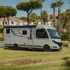 Das vollintegrierte Luxus-Wohnmobil Hymer B-Klasse Master-Line steht auf einer Rasenfläche vor Palmen im Sonnenschein.