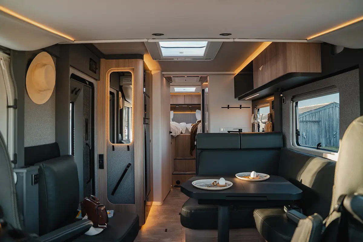Moderner Innenraum des Hymer B-Klasse Wohnmobils mit dunkler Sitzgruppe, edler Beleuchtung und Blickachse nach hinten zum Heckbett.