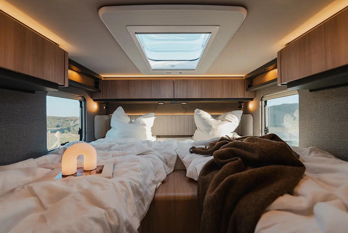 Blick auf die gemütlichen Einzelbetten im Heck des Hymer Wohnmobils mit umlaufenden Hängeschränken und indirektem LED-Licht.