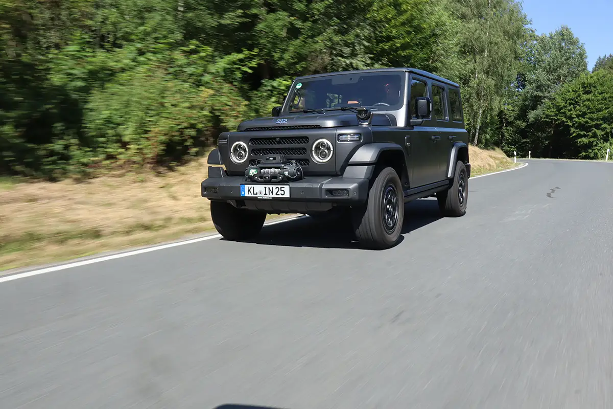 Schrägansicht von vorne auf den BAW 212 bei zügiger Fahrt auf einer asphaltierten Strasse im Wald.