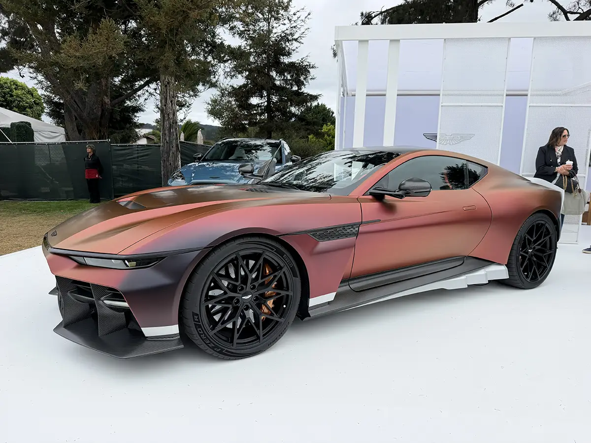 Seitenprofil des kupferrot schimmernden Aston Martin Valen mit Carbon-Karosserie auf dem Präsentationspodest im Freien.