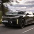 Ein tiefschwarzer Lucid Gravity Grand Touring in der Farbe Abyss Black fährt dynamisch auf einer asphaltierten Bergstrasse vor einer Hügelkulisse.