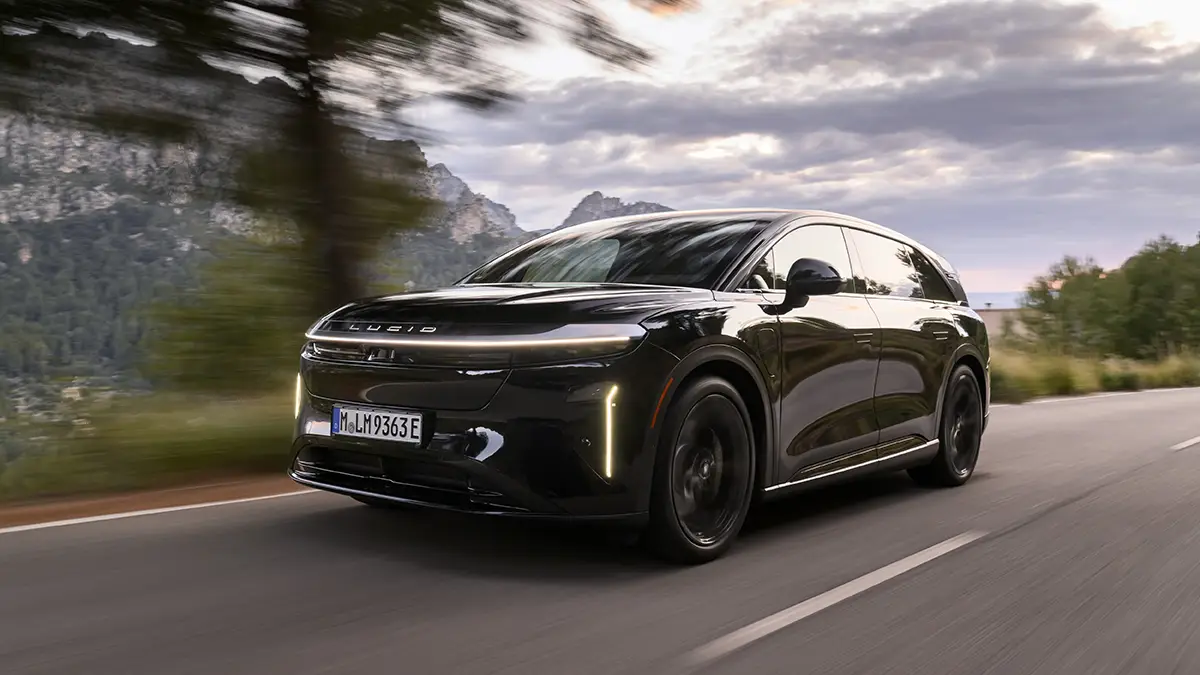Ein tiefschwarzer Lucid Gravity Grand Touring in der Farbe Abyss Black fährt dynamisch auf einer asphaltierten Bergstrasse vor einer Hügelkulisse.