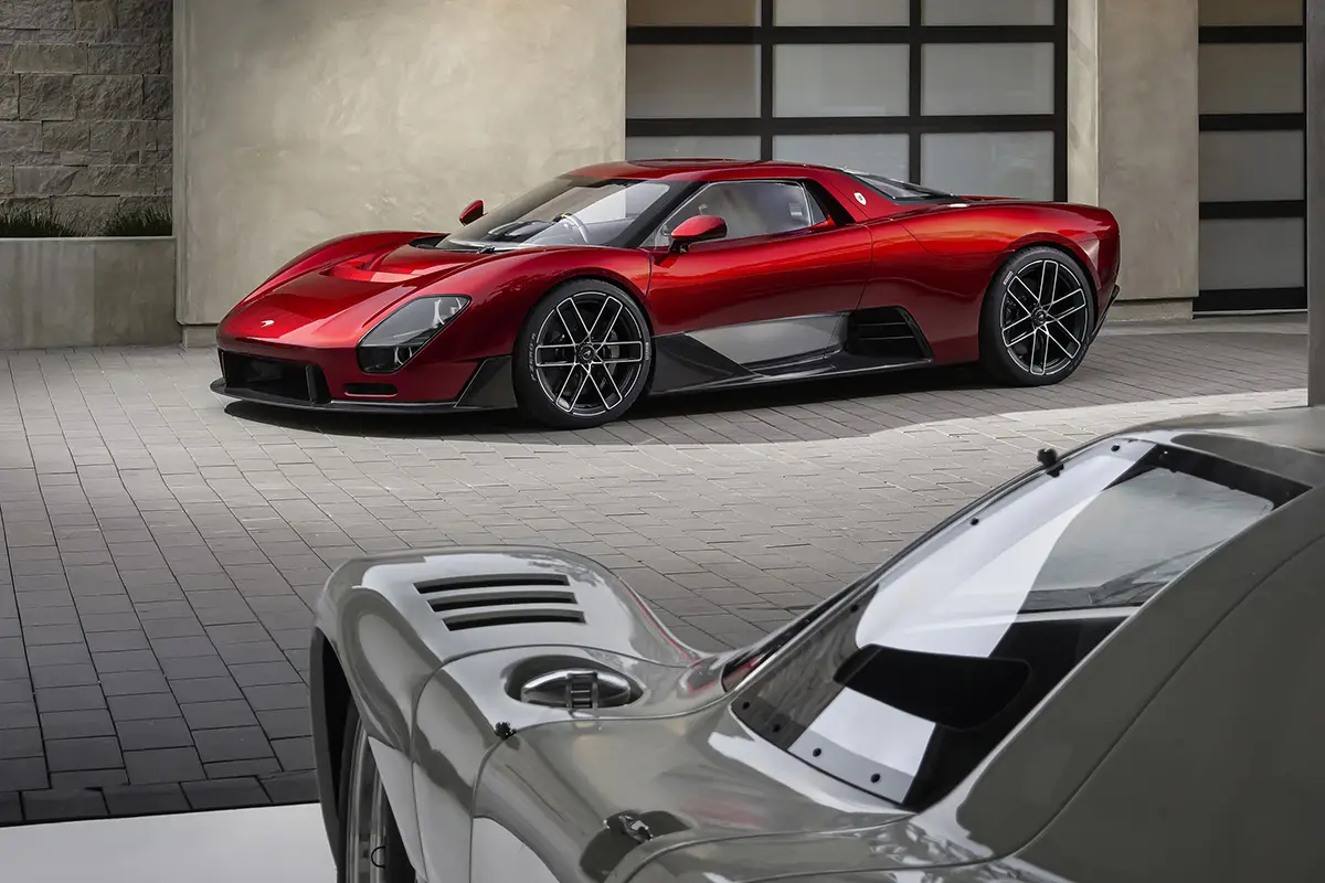 Der rote McLaren McL 6GT Konzeptwagen im Hof neben dem historischen McLaren M6GT Rennwagen im Vordergrund.