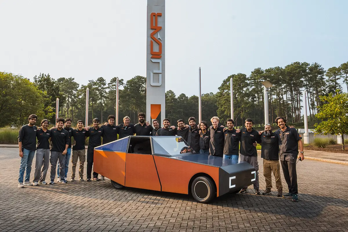 16 Masterstudierende der Clemson University posieren stolz hinter dem entwickelten orange-grauen Solarauto Luminetta.