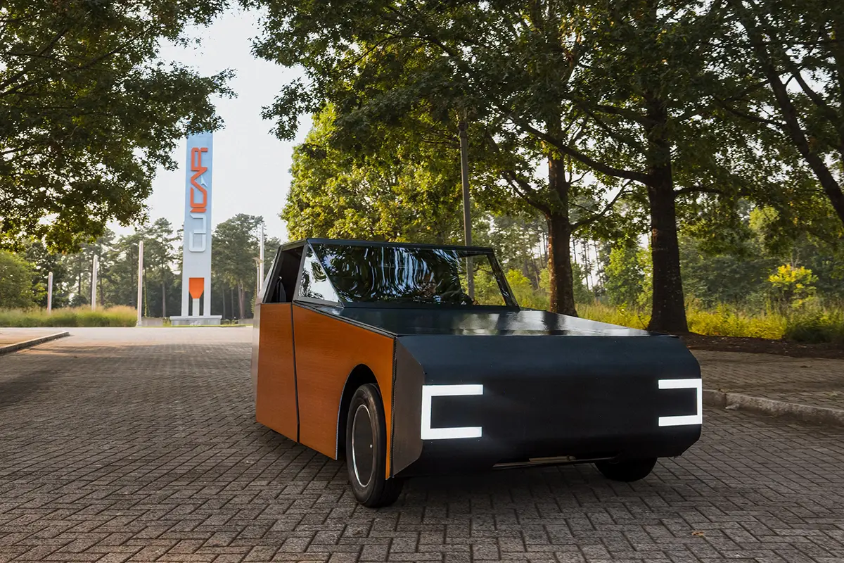 Frontalansicht des flachen Solarautos Luminetta mit C-förmigen LED-Scheinwerfern auf Pflasterstein.