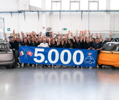 Die gesamte Belegschaft des AMFI-Werks in Turin jubelt mit erhobenen Händen hinter einem 5'000-Banner neben dem bronzenen Jubiläums-Microlino. Foto: Microlino