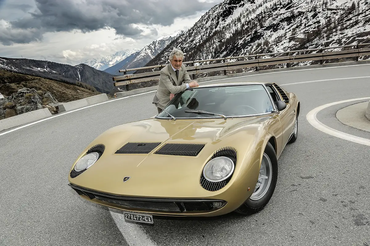 Goldener Lamborghini Miura P400 auf einer alpinen Passstraße vor felsiger Bergkulisse