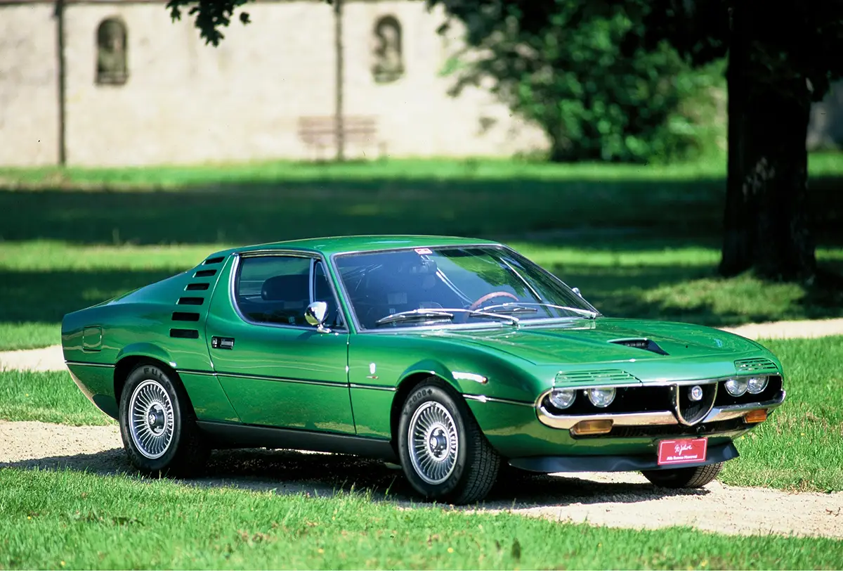 Grünes Sportcoupé Alfa Romeo Montreal mit markanten Scheinwerferblenden auf einer Wiese
