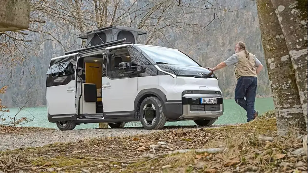 Alpincamper Kia PV5 mit geöffneter Schiebetür in freier Natur am Ufer eines Sees mit Person an der Motorhaube.