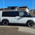 Weisser Alpincamper Kia PV5 Elektro-Minicamper mit aufgestelltem Reimo-Hubdach in der Seitenansicht auf Asphalt.