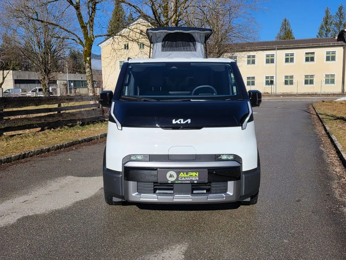 Frontansicht des weissen Alpincamper Kia PV5 Elektrotransporters mit geschlossenem Hubdach auf einer Strasse.