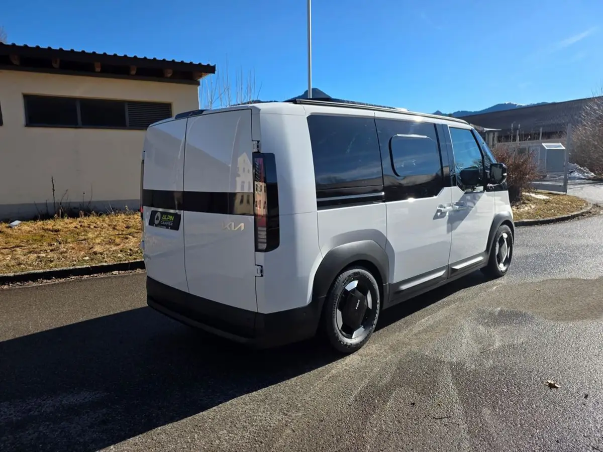 Schrägansicht von hinten auf den weissen Kia PV5 Alpincamper mit getönten Scheiben im Stand.