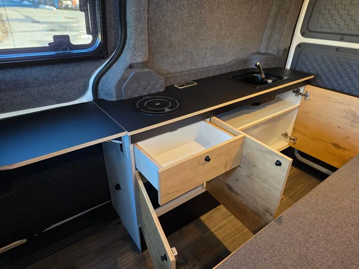 Detailansicht der Küchenzeile im Kia PV5 Alpincamper mit ausgezogenen Schubladen und eingelassenem Induktionskochfeld.