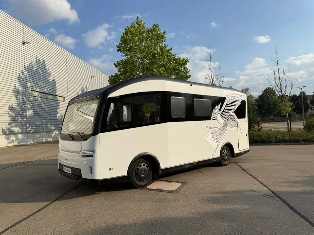 Vollintegriertes Elektro-Wohnmobil CityFreighter Evolve in Weiss mit Schwingen-Dekor vor einem modernen Industriegebäude.