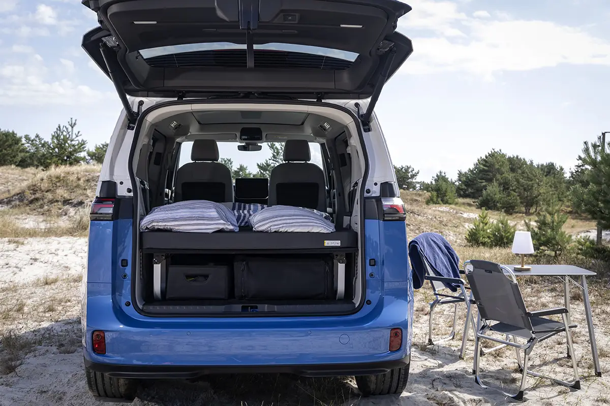 Innenansicht des VW ID.California Cruise mit ausgeklapptem Doppelbett, 9 cm starker Klappmatratze und blau-weisser Bettwäsche.