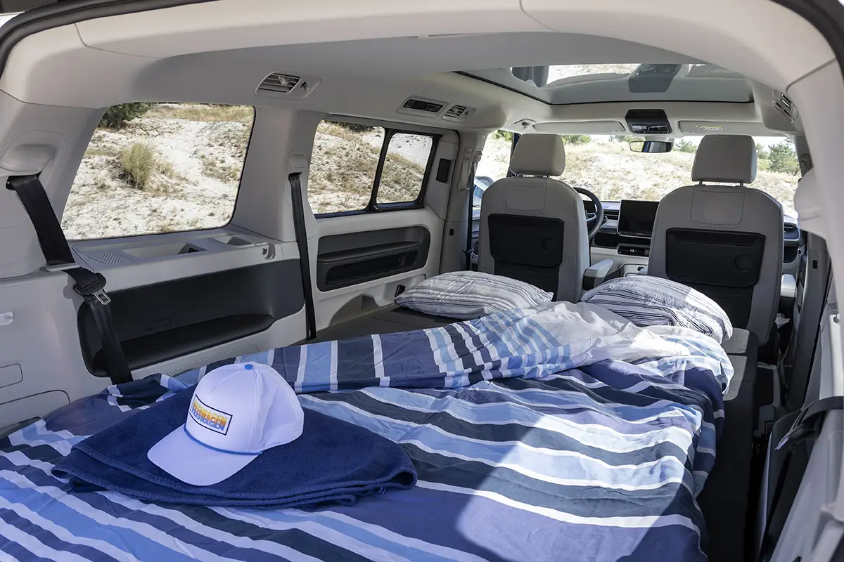 Innenansicht des VW ID.California Cruise mit ausgeklapptem Doppelbett, 9 cm starker Klappmatratze und blau-weisser Bettwäsche.