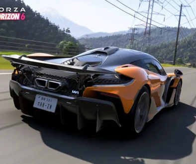 Papaya-oranger McLaren W1 Supersportwagen in dynamischer Fahrt auf einer Landstrasse mit Blick auf schneebedeckte Berge im Rennspiel Forza Horizon 6.