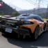 Papaya-oranger McLaren W1 Supersportwagen in dynamischer Fahrt auf einer Landstrasse mit Blick auf schneebedeckte Berge im Rennspiel Forza Horizon 6.
