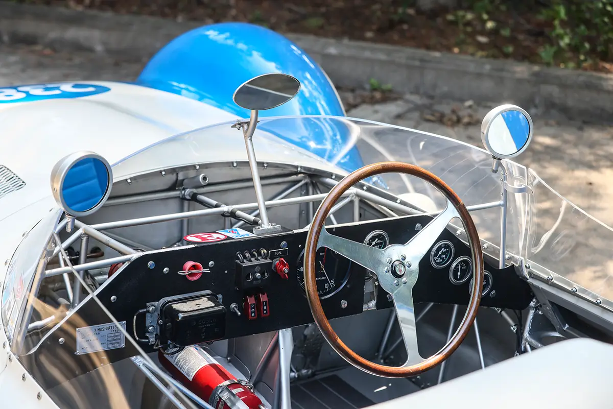 Fahrerperspektive auf das minimalistische Renn-Armaturenbrett mit Rundinstrumenten, Kippschaltern und Holzlenkrad im Tipo 61.