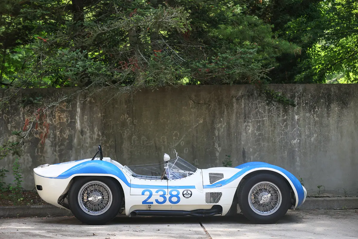 Vollständige Seitenansicht des weiss-blauen Maserati Tipo 61 Birdcage Rennwagens mit Startnummer 238 im Profil vor einer Betonwand.