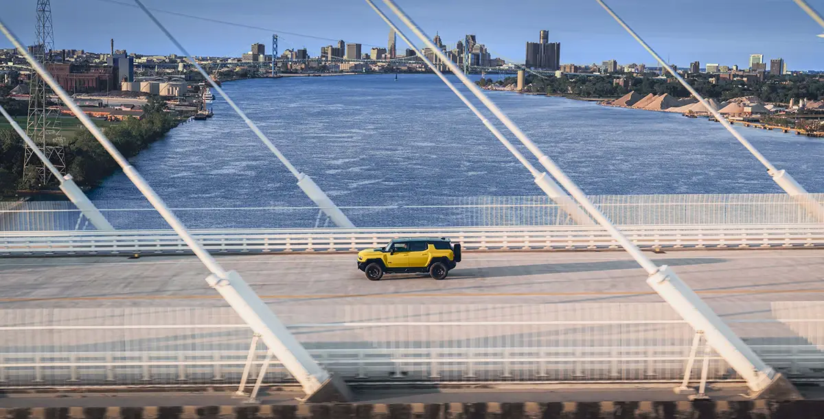 Luftaufnahme eines gelben GMC Hummer EV bei der Überquerung einer weitgespannten Schrägseilbrücke über einen breiten Fluss
