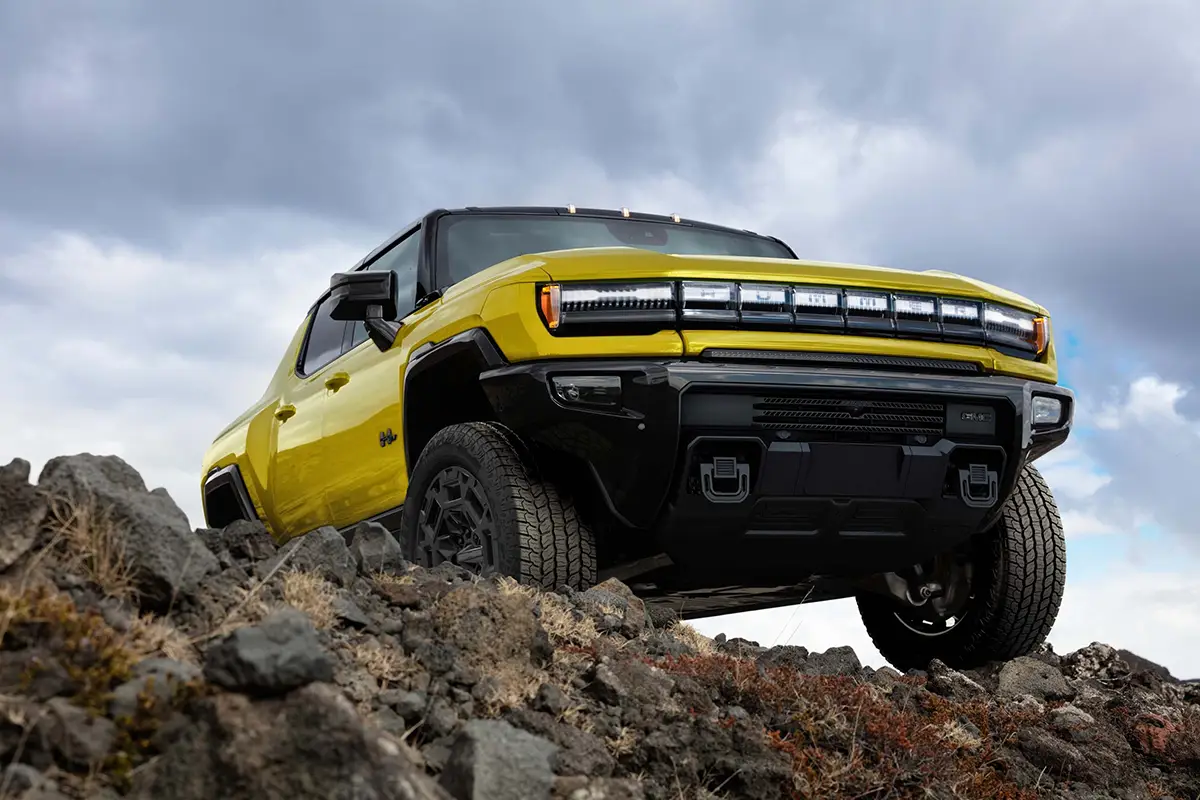 Gelber GMC Hummer EV Pickup klettert im steilen Gelände über grobe Felsen unter bewölktem Himmel