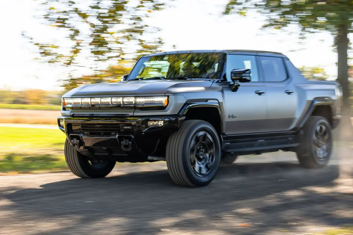 Dunkelgrauer GMC Hummer EV 3X Pickup in zügiger Fahrt auf einer ländlichen Schotterstrasse mit aufwirbelndem Staub