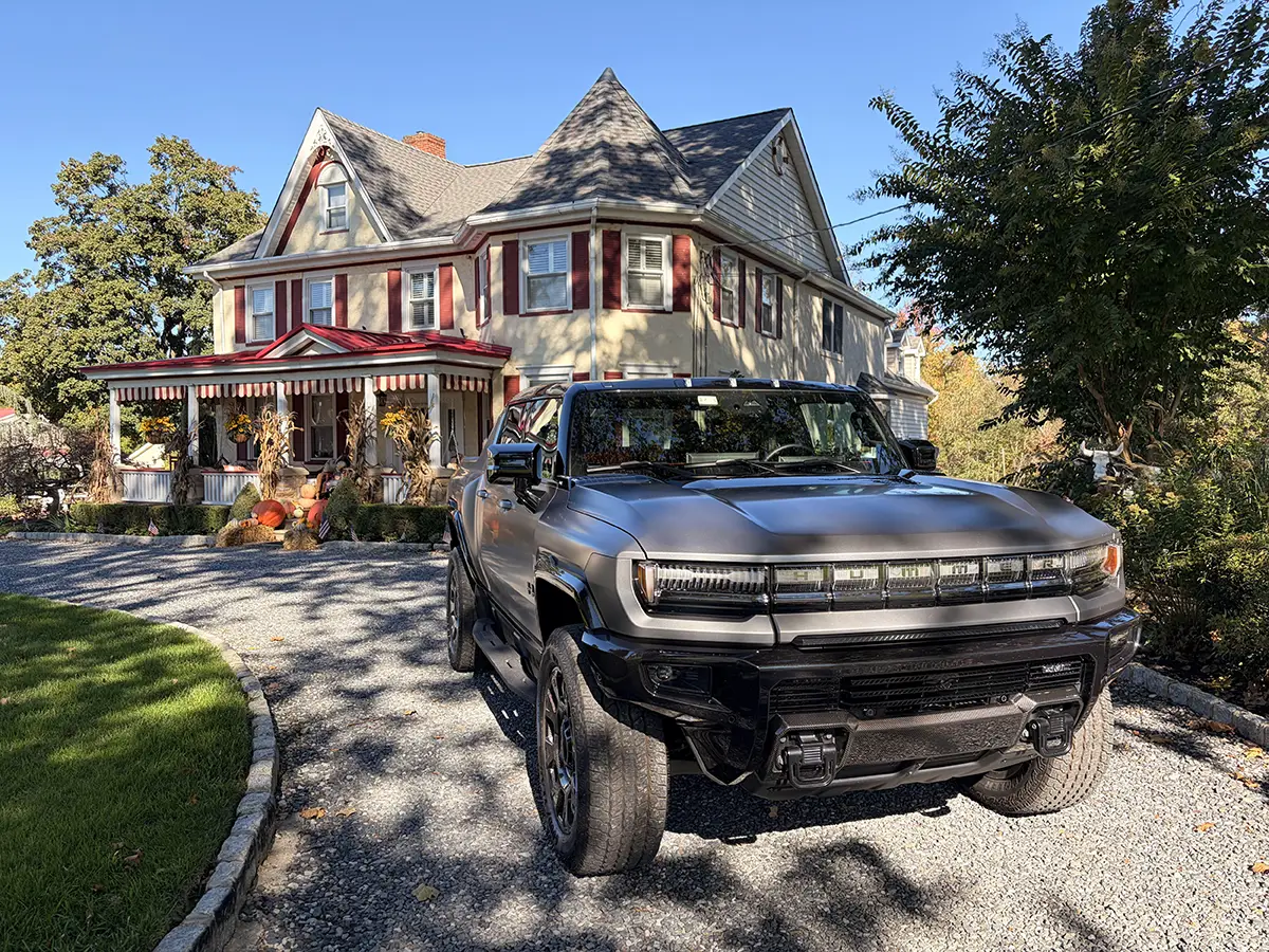 Dunkler GMC Hummer EV Pickup in der Kiesauffahrt vor einer herrschaftlichen amerikanischen Villa mit Veranda