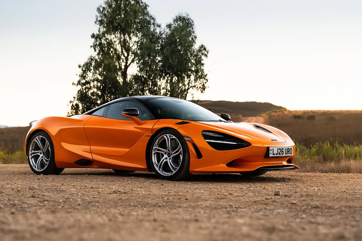 Orangener McLaren 750S Coupé mit schwarzen Akzenten und silbernen Alufelgen in Schrägansicht von vorn in der Abendsonne